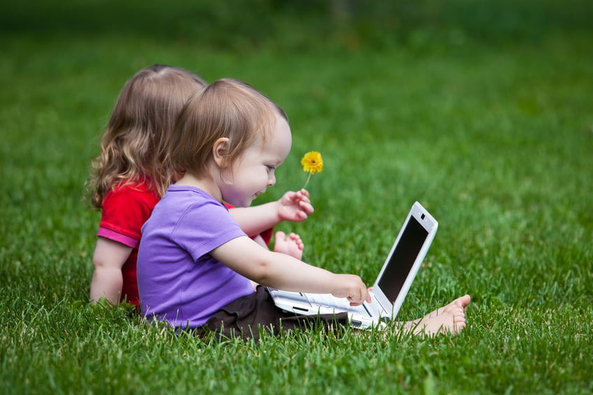 Two little children working together on the meadow with a laptop.