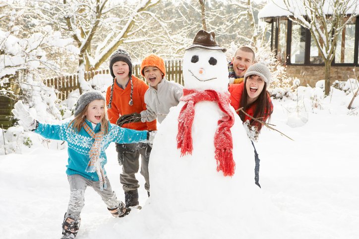 Family Having Fun Building Snowman In Garden