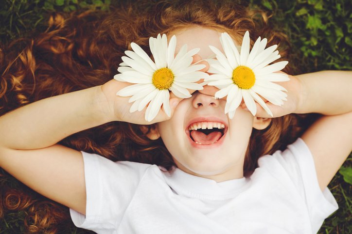 Child with daisy eyes, on green grass in a summer park.