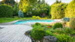 Backyard rock garden with outdoor inground residential swimming pool, curved wooden deck and stone patio