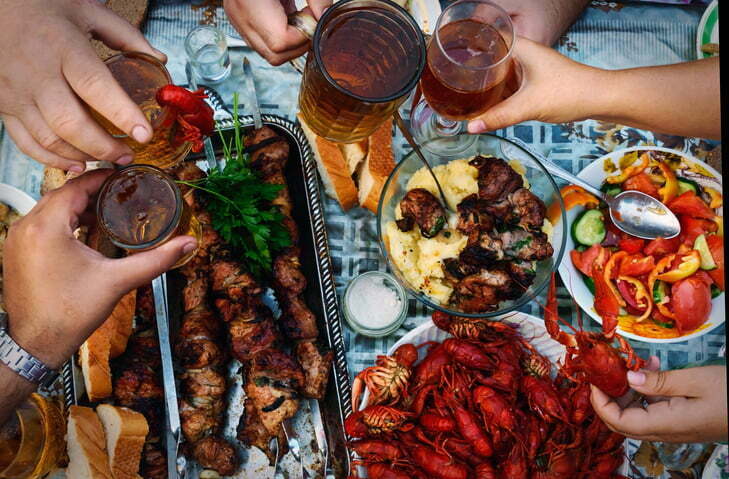 Feast of beer, meat skewer and crayfish. The top view on the group of people who dine outdoors.